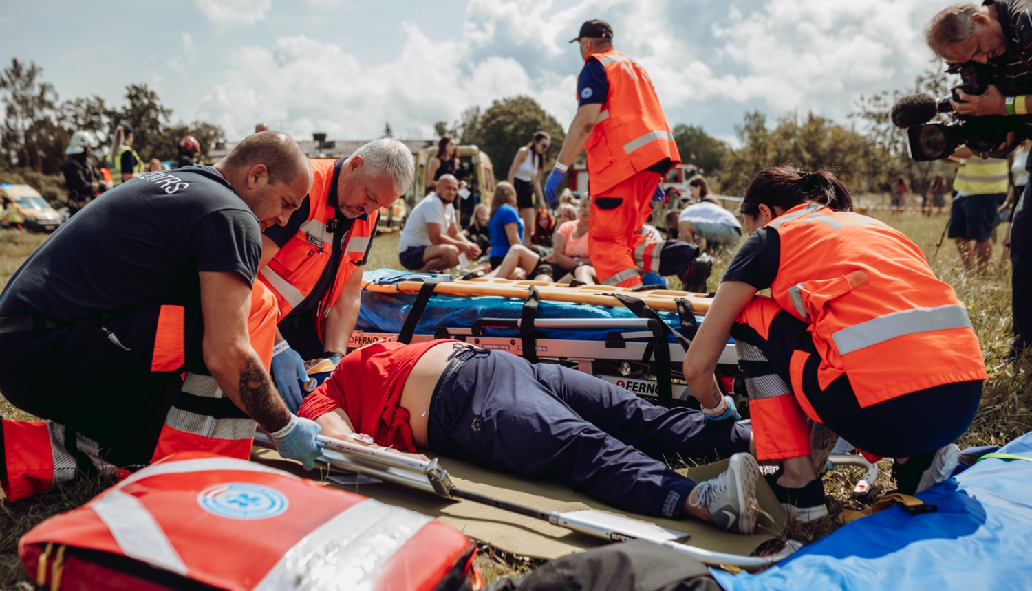 NMPD mediķi mācībās sniedz palīdzību. Apkārt 4 mediķi oranžās formās, priekšplānā soma